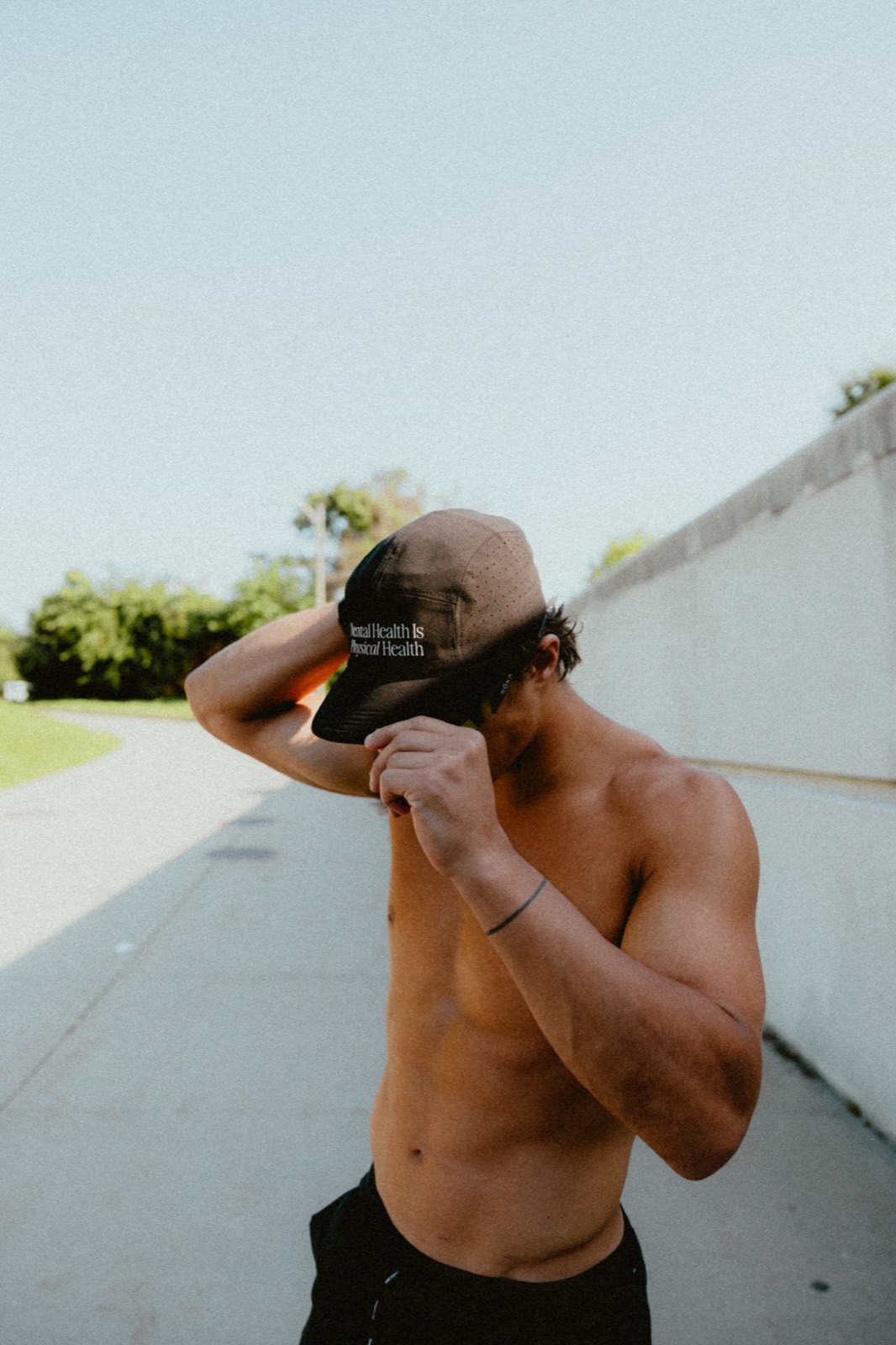 Logan adjusting a Tmrrw Project cap reading “Mental Health Is Physical Health” on a sunny path